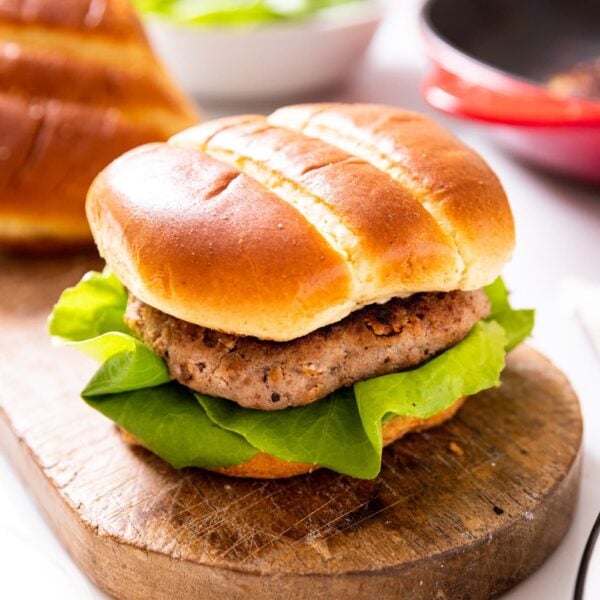 Turkey burger with slice of lettuce sitting in brioche bun all on wood board on white countertop