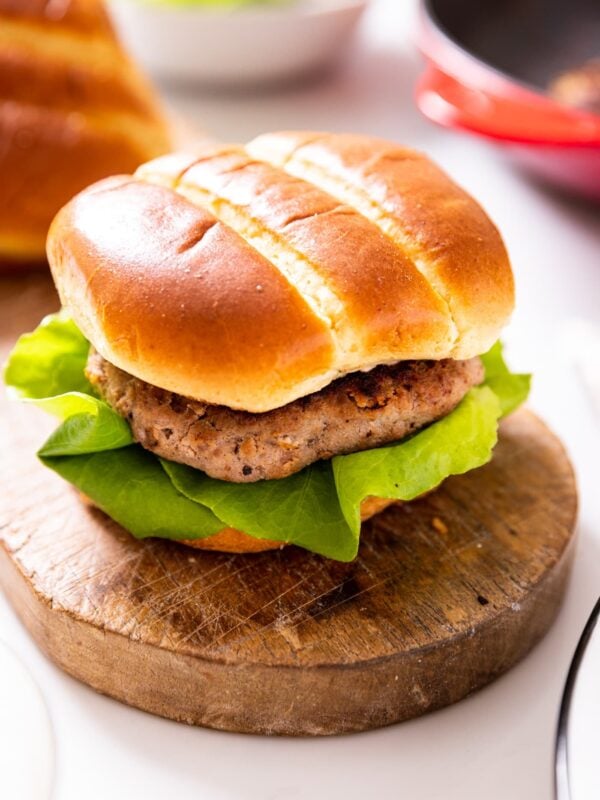 Turkey burger sandwiched in a brioche bunk with a piece of lettuce sitting on wood board with red skillet in background