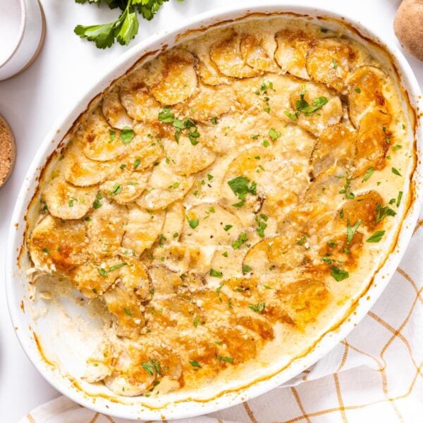Top down view of white baking dish filled with scalloped potatoes topped with parsley all on white countertop