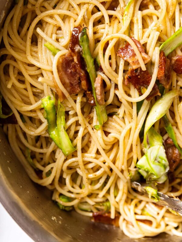Top down view of metal pot filled with brown butter spaghetti with bacon and slices of asparagus