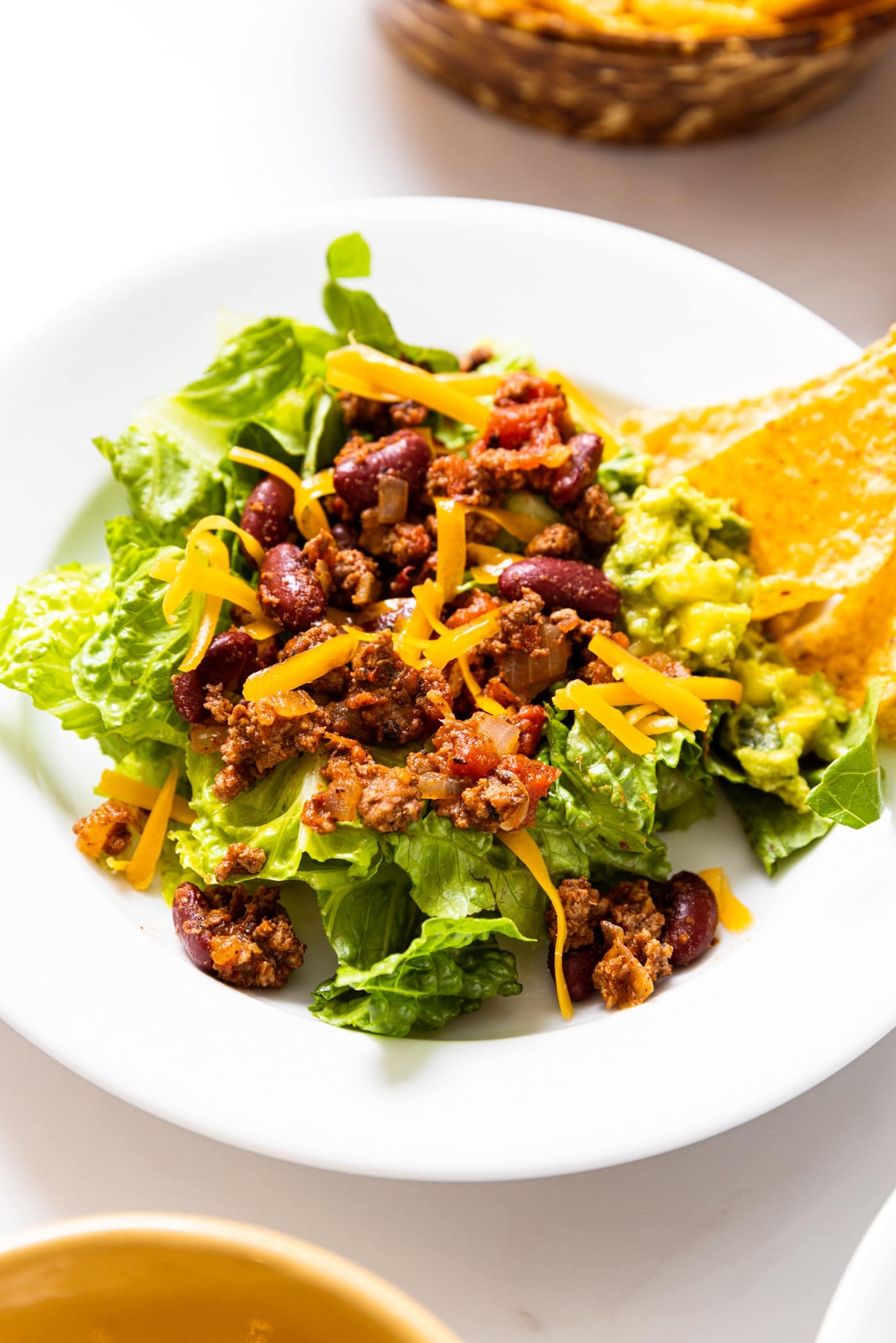 White plate filled with a classic taco salad with dressing, cheese, and chips served to the side.