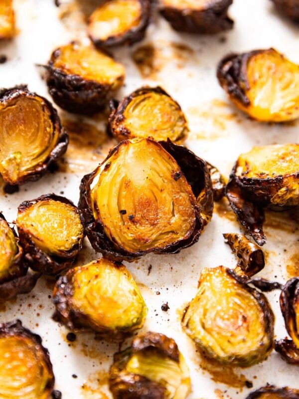 Crispy honey Brussels sprouts sitting on white baking sheet after being charred in the oven