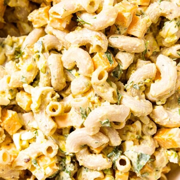 Top down view of bowl filled with macaroni salad with cubes of cheese and herbs