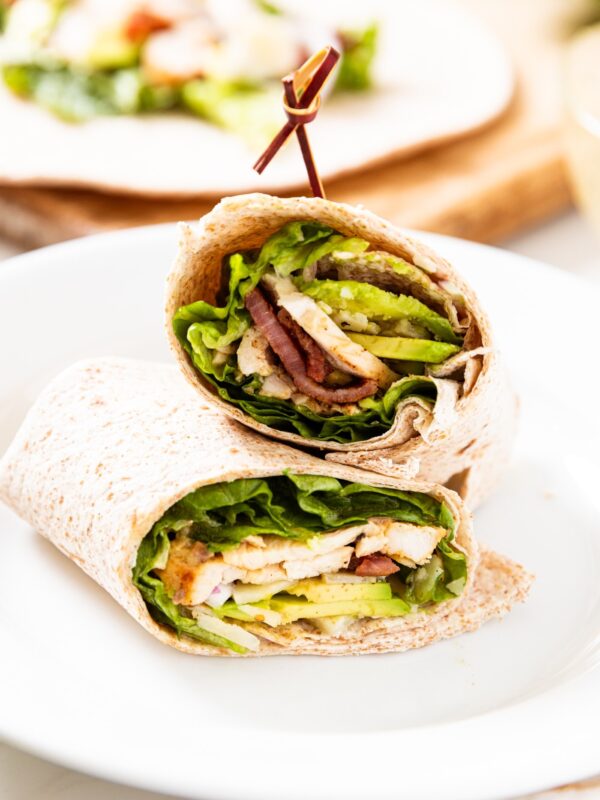 One grilled chicken wrap in flour tortilla cut in half and stacked on top of each other with toothpick in top half.