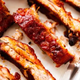 Baby back ribs dripping in sauce sitting on metal baking rack with more sauce to the side.