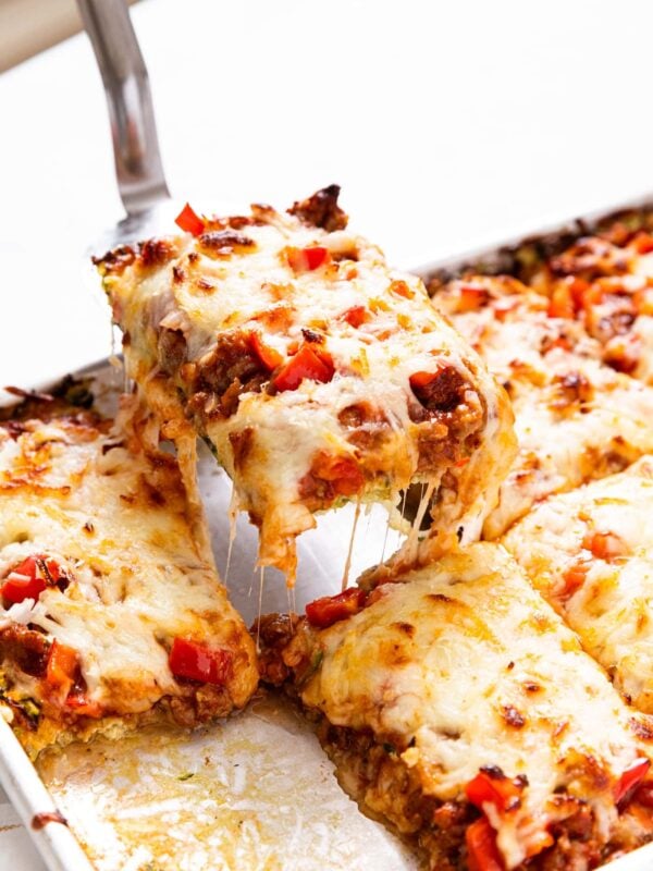 Spatula pulling piece of zucchini crust pizza from pan with other slices of pizza with pieces of cheese clinging to pizza below.