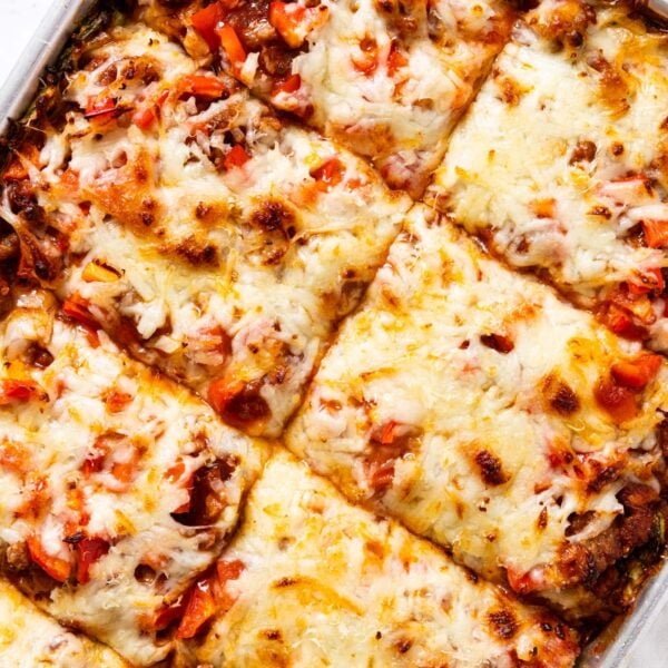 White marble countertop with metal sheet pan sitting on surface filled with zucchini crust pizza topped with cheese, sausage, and red bell pepper.