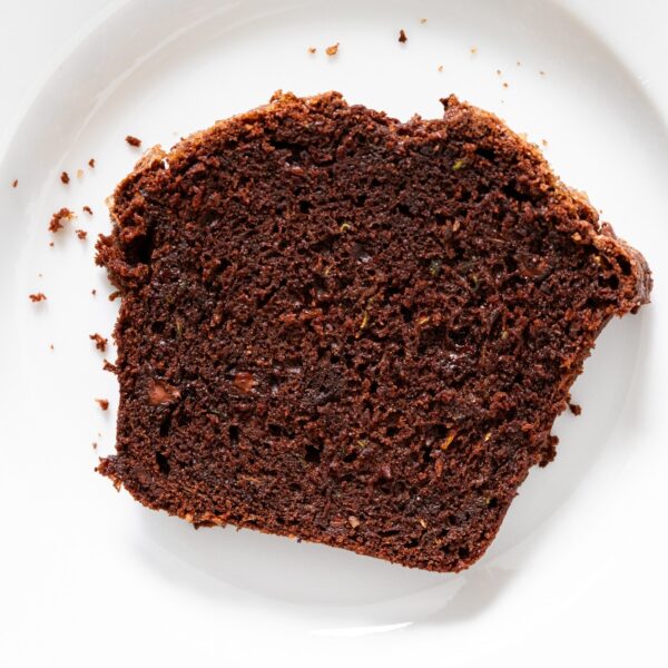 White plate with slice of chocolate zucchini bread sitting on it with crumbs from the bread on the plate.