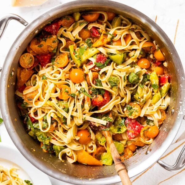 Large metal stockpot filled with pasta mixed with herbs and tomatoes all on marble surface.