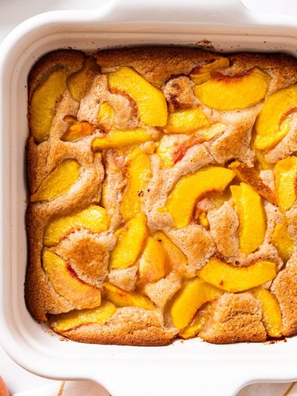 White baking dish filled with baked lazy peach cobbler with slices of peaches on top.