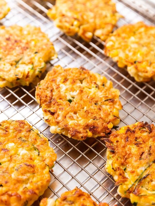 Zucchini corn fritters sitting on wire cooling rack after being browned in a skillet on the heat with crispy brown edges all over.