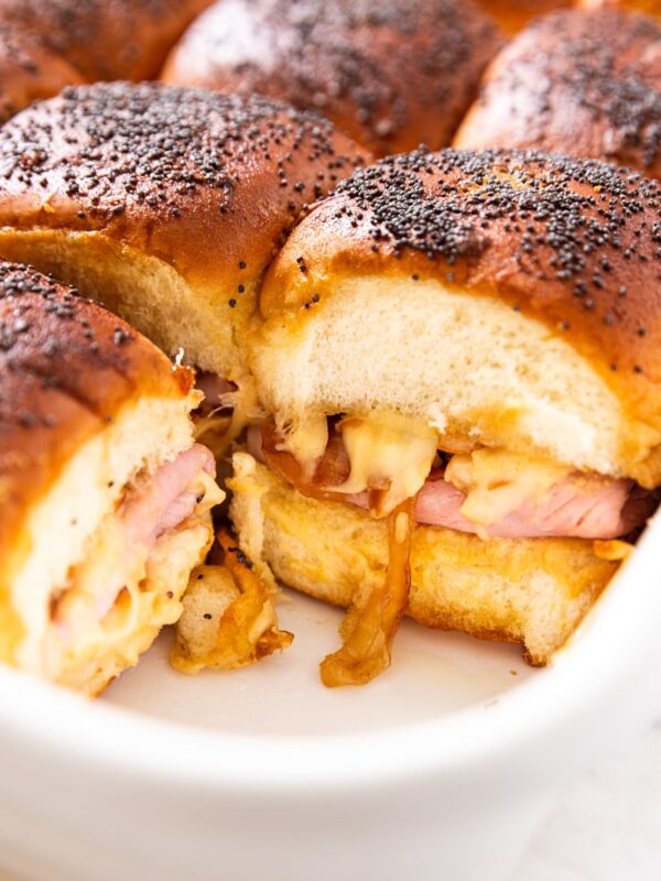 Ham and cheese sliders in white baking dish after coming out of the oven showing melted cheese and caramelized onions.