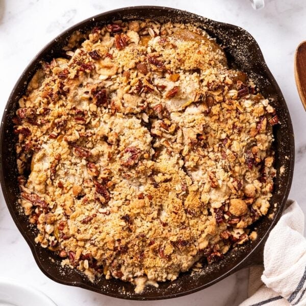 Baked pear crisp sitting in black skillet on marble surface with towel wrapped around hot handle.