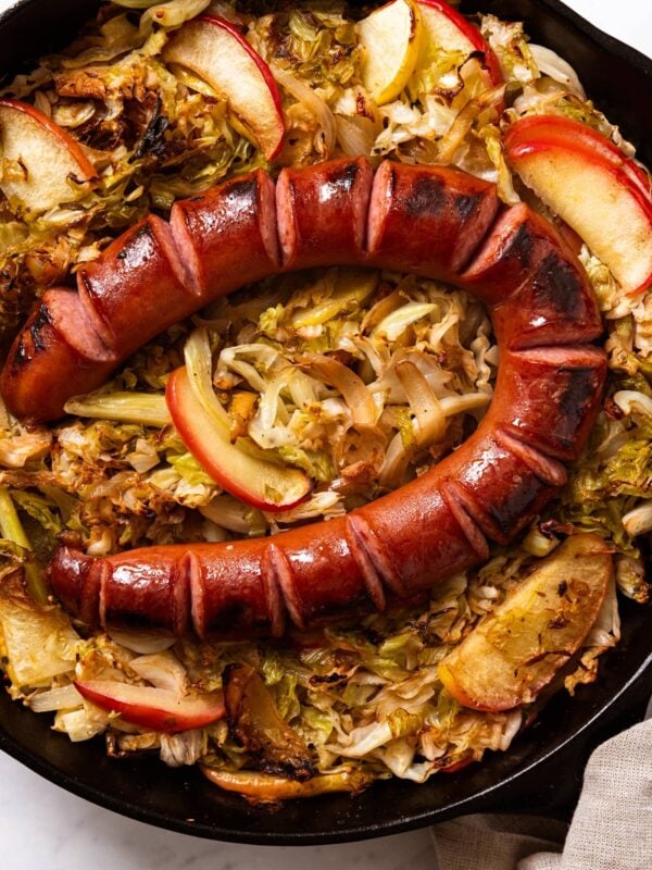 Black cast iron skillet filled with cooked cabbage and apple with browned piece of kielbasa nestled on top.