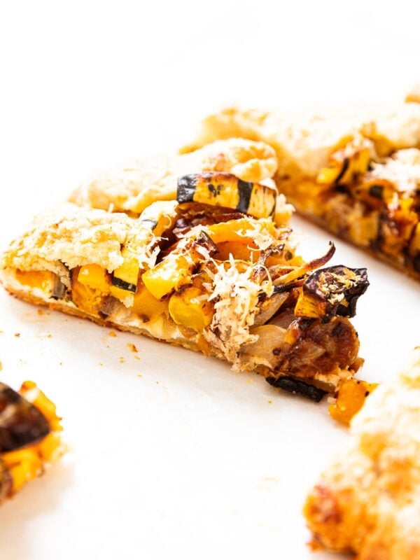 White surface with a slice of squash galette with caramelized vegetables on top with other slices all around.