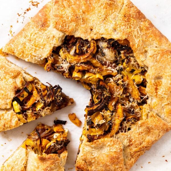Baked savory squash galette sitting on white piece of parchment paper showing pieces of squash and onion.