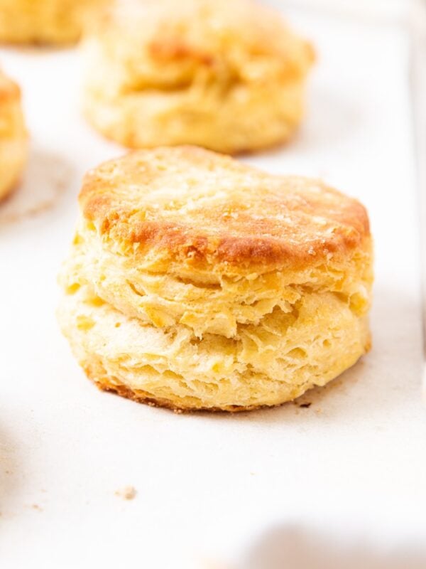Buttermilk biscuits showing flaking interiors sitting on white piece of parchment after being baked in the oven.