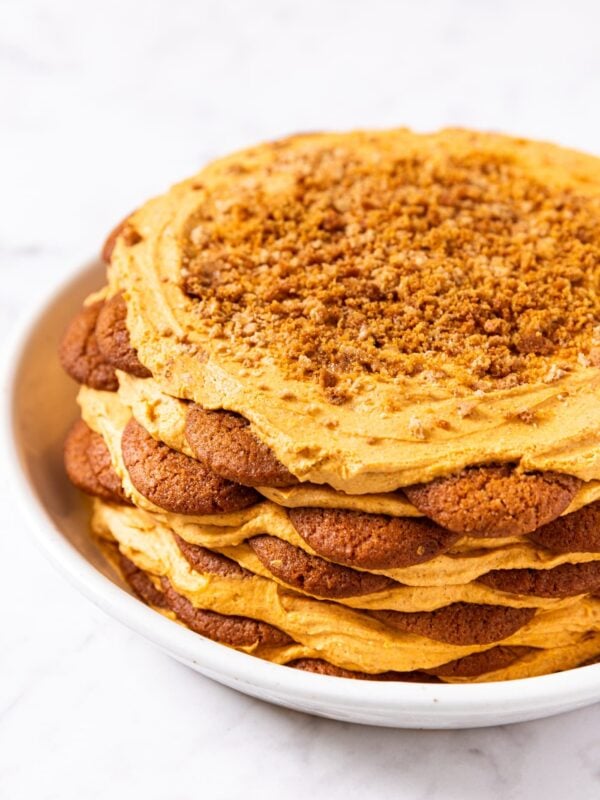 Pumpkin icebox cake with pumpkin whipped topping all over the top with gingersnap crumble on top sitting in white serving platter.