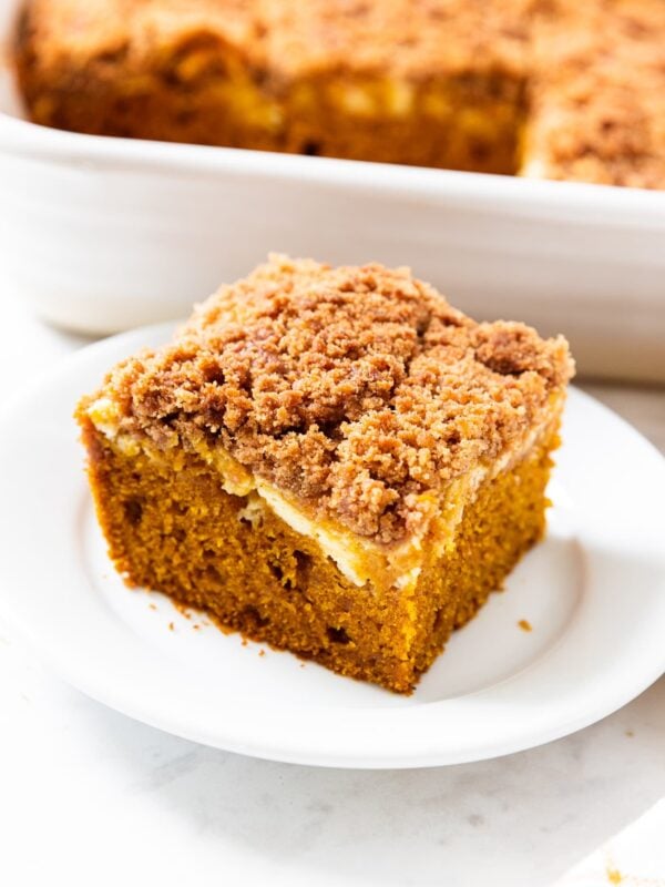 Small white plate with square piece of pumpkin coffee cake with swirl of cheesecake filling with streusel topping.