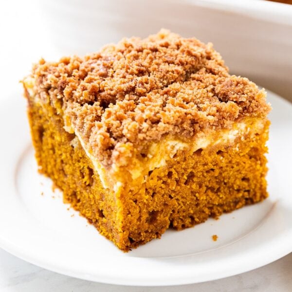 White plate with square of pumpkin coffee cake with cheesecake swirl layer with baking dish in background.
