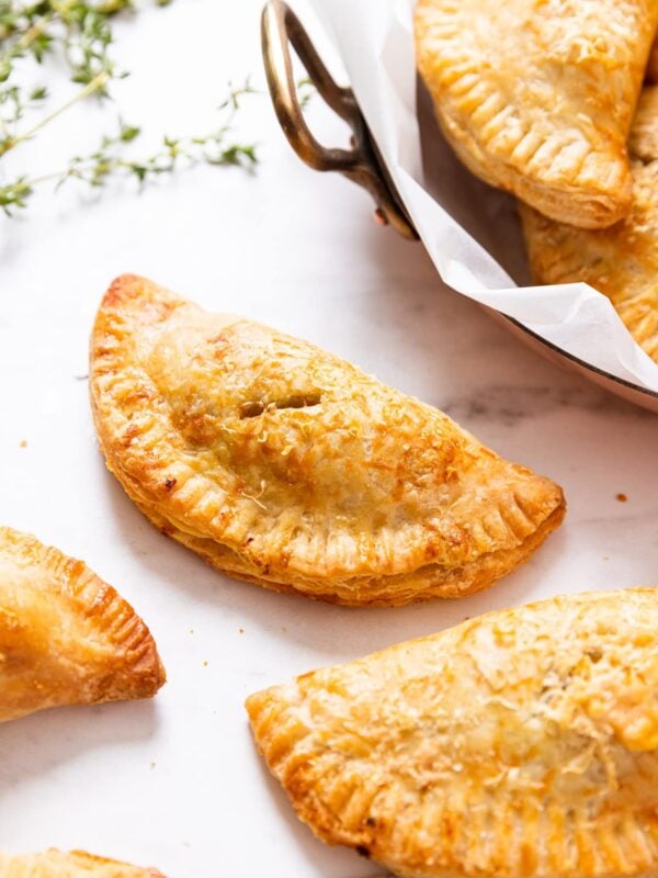 Baked half moon shaped savory squash hand pies sitting on marble surface with fresh thyme in background and more hand pies sitting on a copper piece to the side.