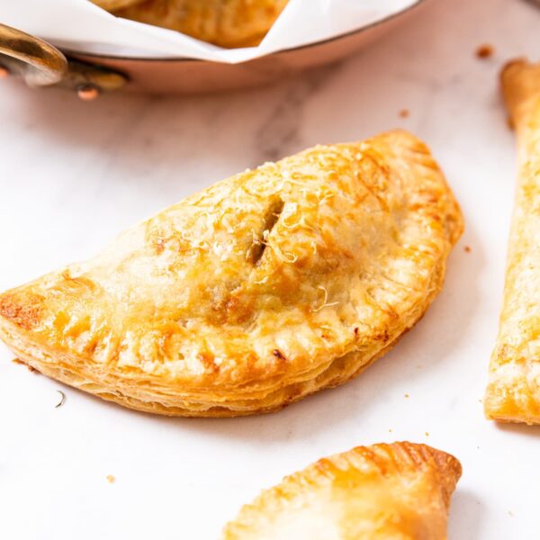 Savory squash hand pie sitting on marble surface after being browned in the oven while baking with more hand pies to the side and in background.
