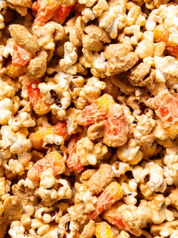 Peanut butter covered popcorn sitting on baking sheet with pieces of candy corn and peanuts.