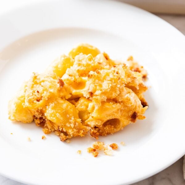 White plate filled with serving of macaroni & cheese with breadcrumb topping with a few crumbs on the side of the plate.