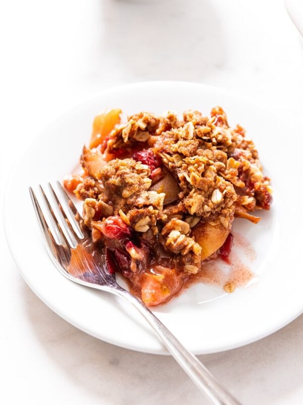 White plate filled with scoop of cranberry with fork resting on side of plate with coffee cup in background all on white marble surface.