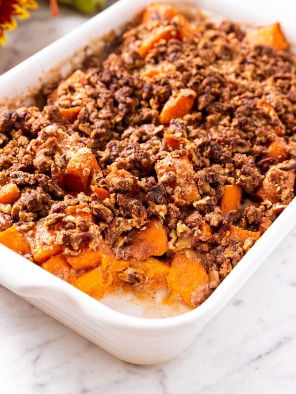 White baking sheet filled with sweet potato casserole topped with streusel topping with one scoop missing all on white marble surface.