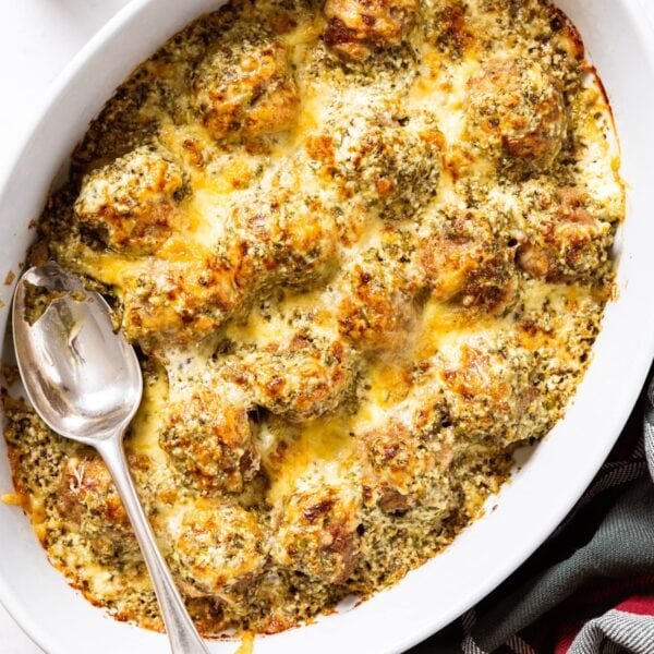 Oval white baking dish sitting on marble surface filled with baked meatballs topped with melted cheese with holiday-themed napkin to the side.