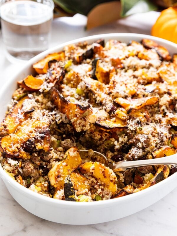 White baking dish sitting on white marble surface with spoon scooping out serving of the acorn squash casserole topped with Parmesan cheese.