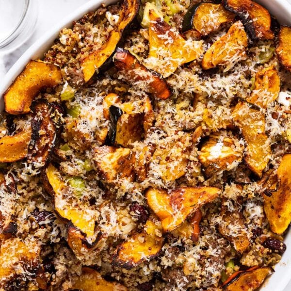 White baking dish sitting on white marble surface filled with baked acorn squash casserole topped with browned pieces of squash and shredded Parmesan cheese.