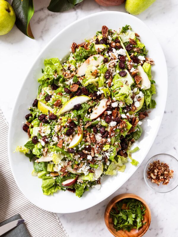 White marble surface with white serving platter filled with wild rice salad and topped with pear and dried cranberries and feta cheese with magnolia garland along the top.
