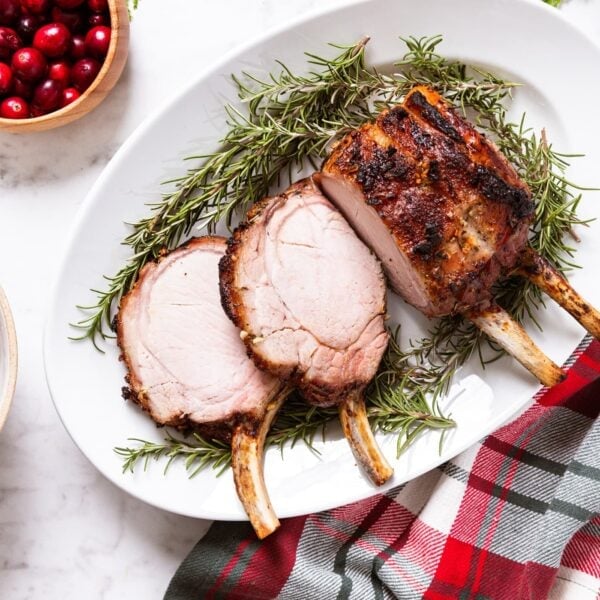 Oval white platter filled with roasted pork rib roast with two slices cut off with rosemary stuck underneath all on white marble countertop with festive napkin.