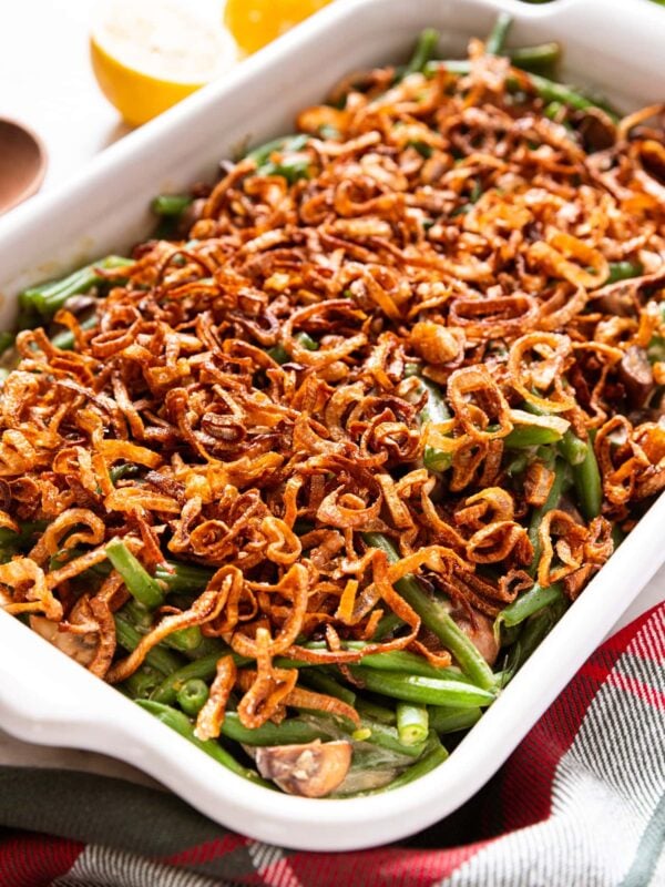 White baking dish filled with green bean casserole topped with crispy fried scallions after coming out of the oven all on white marble surface with half lemons in background.