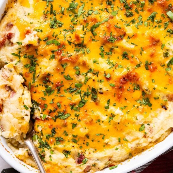 White baking dish filled with baked twice baked potato casserole with browned top sitting on white marble surface.