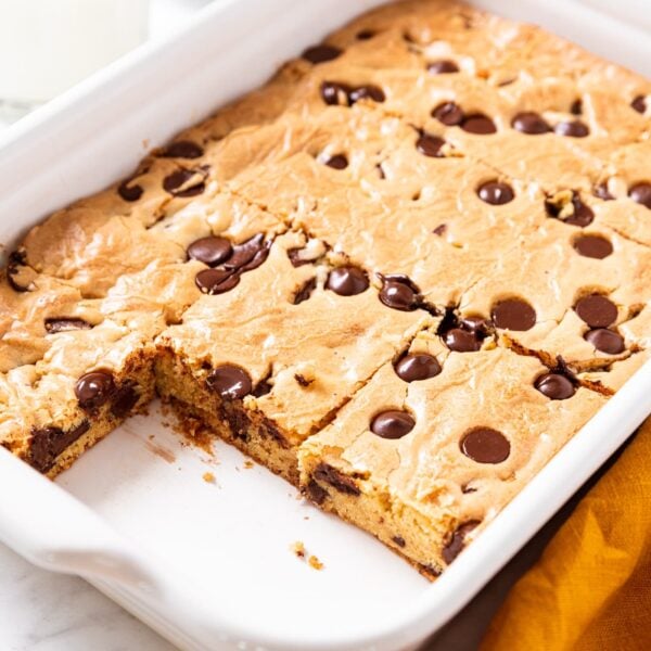White baking dish filled with baked blondies with two pieces removed showing the interior texture of the dessert with yellow napkin to the side.