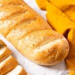 White marble surface with loaf of French bread with linen napkin to the side as well as some sliced bread.