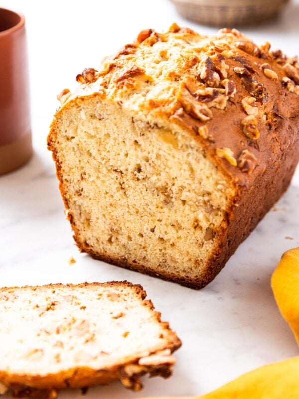 White surface with classic banana bread with a few slices sitting to the side showing interior texture of the bread.
