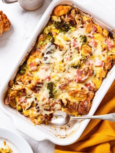 White marble surface with white casserole dish just after coming out of the oven with spoon resting on bottom after scooping out a serving.
