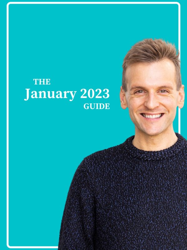 Kaleb Wyse wearing a dark navy blue sweater standing in front of bright blue background smiling.