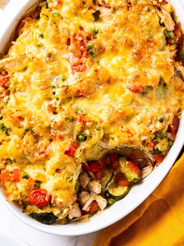 White oval baking dish sitting on marble surface with baked spaghetti squash chicken casserole inside with spoonful missing.