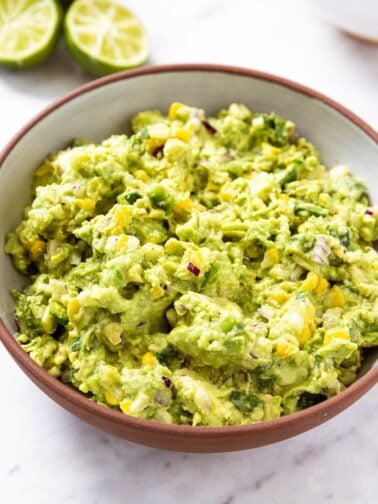 White marble surface with brown bowl filled with sweet corn guacamole with chunky texture.