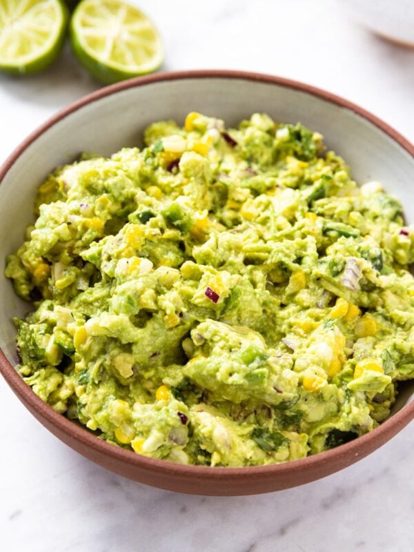 White marble surface with brown bowl filled with sweet corn guacamole with chunky texture.