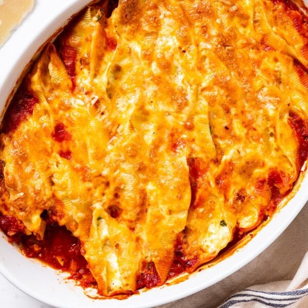 White marble surface with oval white baking dish sitting on top filled with stuffed shells with shredded cheese on top after being melted in oven while baking.