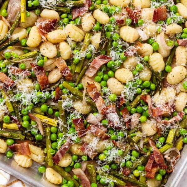 Sheet pan sitting on marble surface with roasted gnocchi, asparagus, bacon, and peas.
