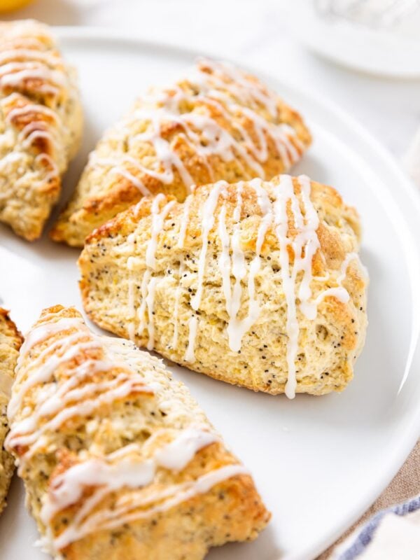 White round platter with lemon poppy seed scones sitting on surface drizzled with white glaze showing interior texture.