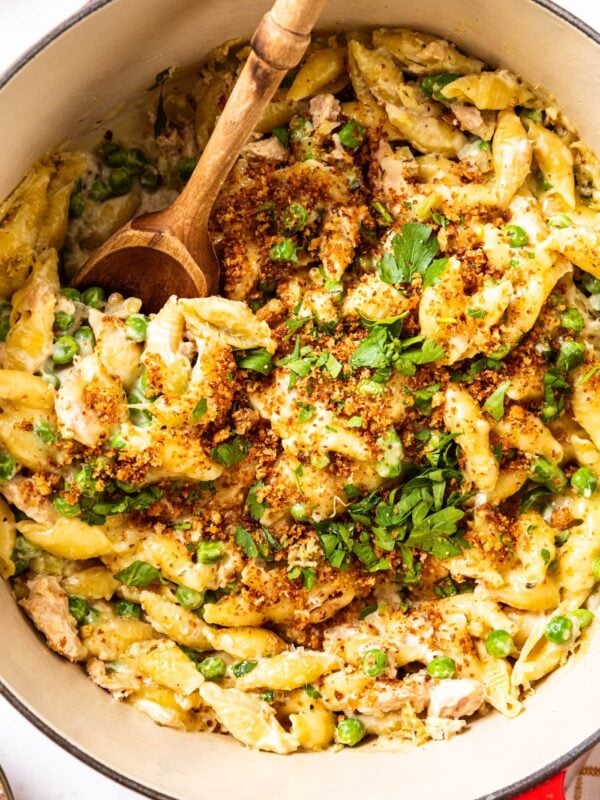 Large pot filled with cooked tuna noodle casserole topped with chopped parsley and browned bread crumbs with spoon about to pull a helping out.