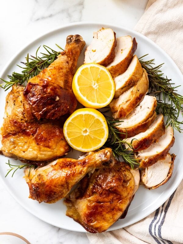 White serving platter filled with pieces of citrus and herb roast chicken with slices of citrus and herbs all around all on piece of white marble.